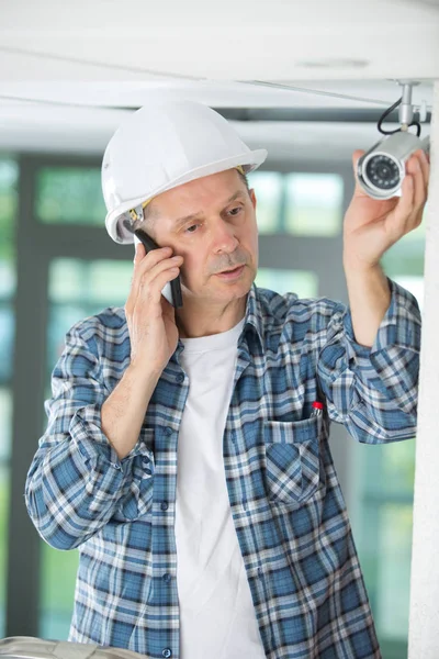 Man using telephone while working on security camera — Stock Photo, Image