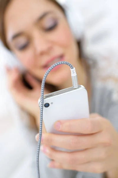 Woman listening to headphones plugged into smartphone — Stock Photo, Image