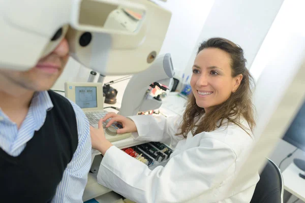 Óptico sonriendo mientras el hombre mira a través de equipos de prueba — Foto de Stock