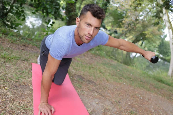 Hombre haciendo ejercicio con pesas en una alfombra al aire libre —  Fotos de Stock