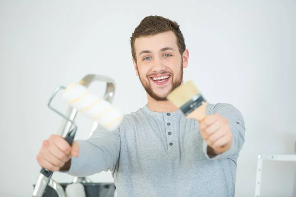 Jovem animado homem segurando pincel de pintura e sorrindo — Fotografia de Stock