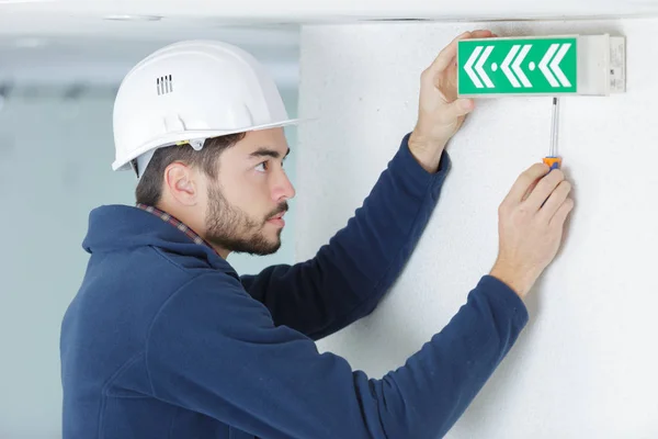 Man fitting illuminated exit sign to wall — Stock Photo, Image