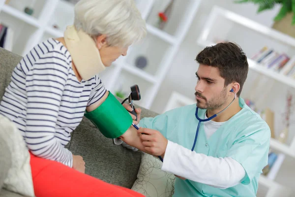 Giovane medico di sesso maschile che prende la pressione sanguigna della donna anziana a casa — Foto Stock