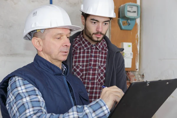 Bouwers met Klembord en elektrische paneel binnenshuis — Stockfoto