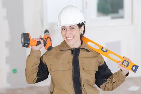 Female builder with spirit level and electric drill — Stock Photo, Image