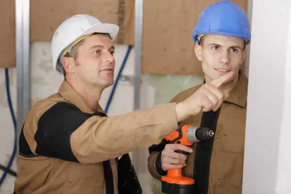 Jefe diciéndole al trabajador dónde usar un taladro eléctrico — Foto de Stock