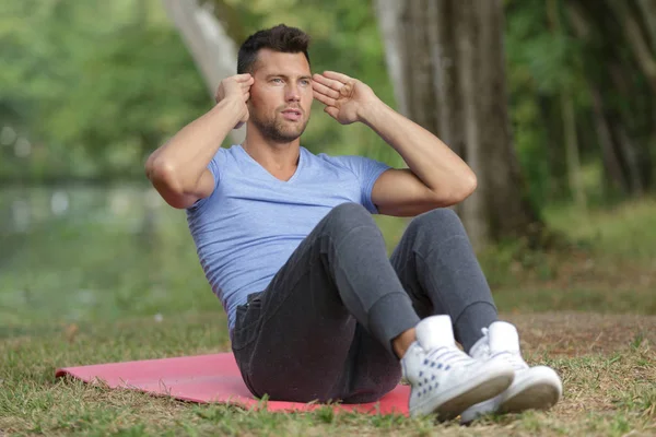 Hombre atractivo está haciendo situps en la hierba fresca —  Fotos de Stock