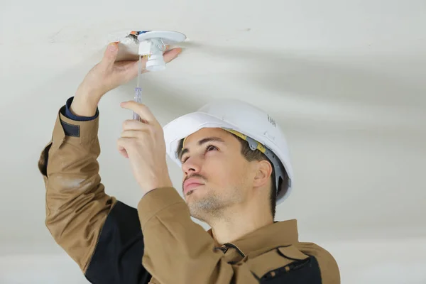 Young electrician mounts round ceiling light in room — Stock Photo, Image