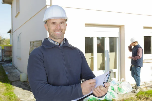 Щасливий будівельний інспектор на будівельному майданчику, що пише на кишені — стокове фото