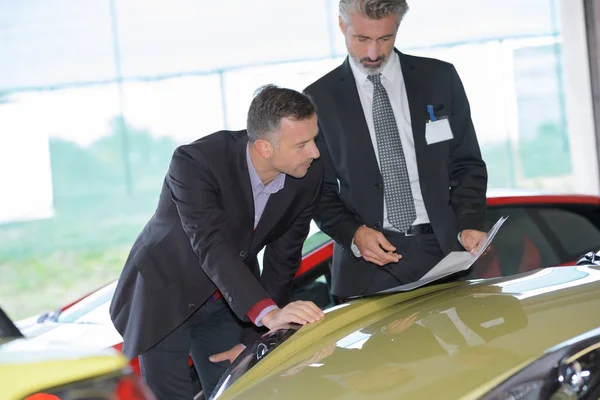 Suited men in sports car showroom — Stock Photo, Image