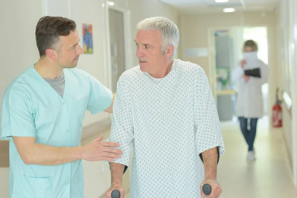 Dokter pria membantu pasien yang lebih tua dengan kruk — Stok Foto