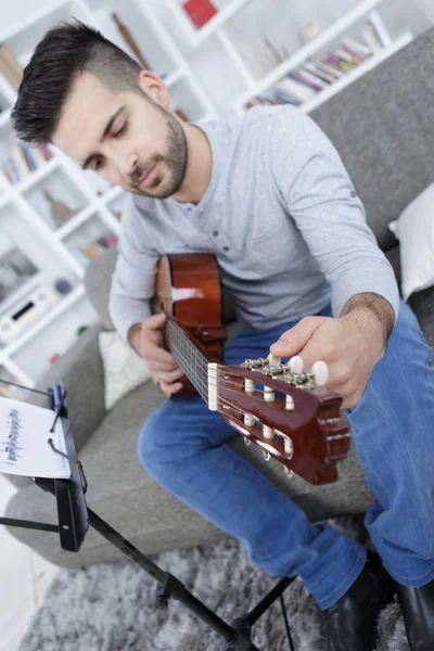 Homem no sofá tocando guitarra em casa — Fotografia de Stock