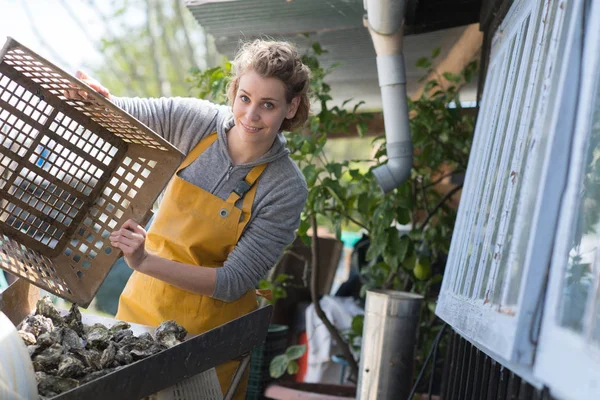 Lächelnde junge Austernarbeiterin zeigt Korb — Stockfoto