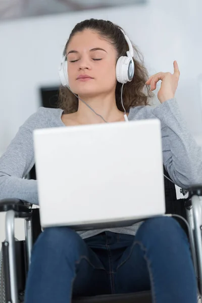 Mujer joven en silla de ruedas escuchando música de la computadora portátil —  Fotos de Stock