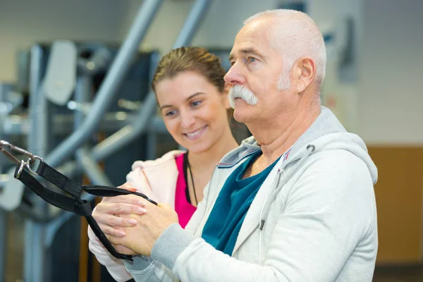 Reifer Mann wurmt sich im Fitnessstudio mit Trainerin — Stockfoto