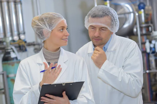 Cientista falando com seu colega segurando prancheta na fábrica — Fotografia de Stock