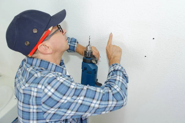 Seniro trabajador hace un agujero en la pared con taladro —  Fotos de Stock