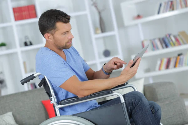 Homem bonito usando um tablet em uma cadeira de rodas em casa — Fotografia de Stock