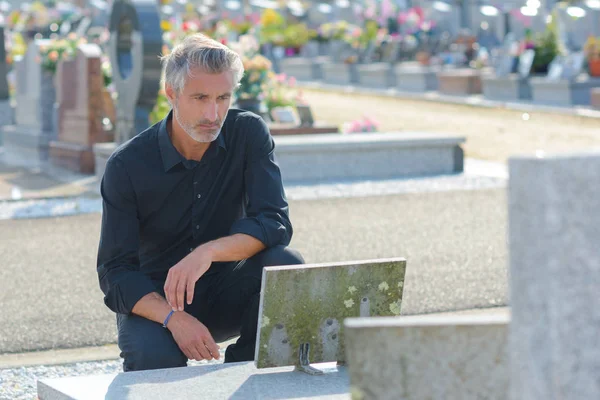 Mann legt Blumen am Grabstein auf Friedhof nieder — Stockfoto