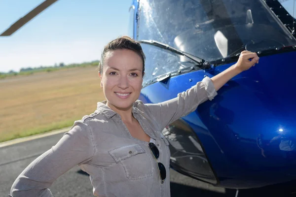 Beautiful woman in pilot overalls resting her arm against helicopter — Stock Photo, Image