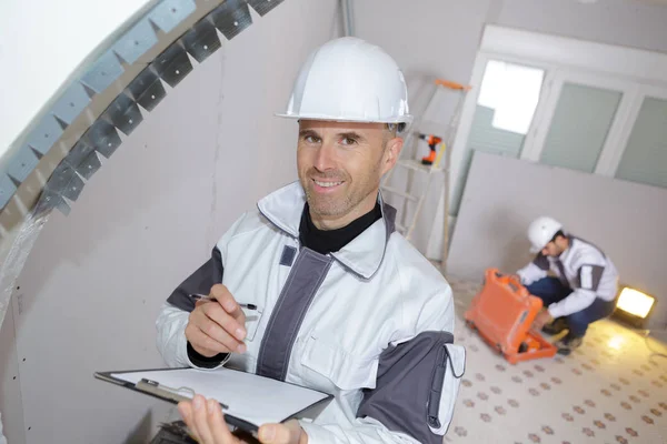Gelukkig bouwer Klembord te houden terwijl u werkt binnenshuis — Stockfoto
