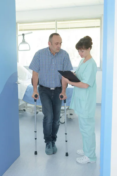 Man on crutches consulting and chatting with a nurse — Stock Photo, Image