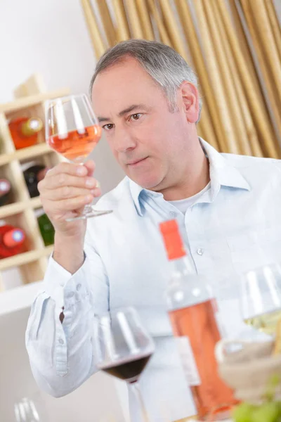 Зрелый мужчина пробует бокал розового вина дома — стоковое фото