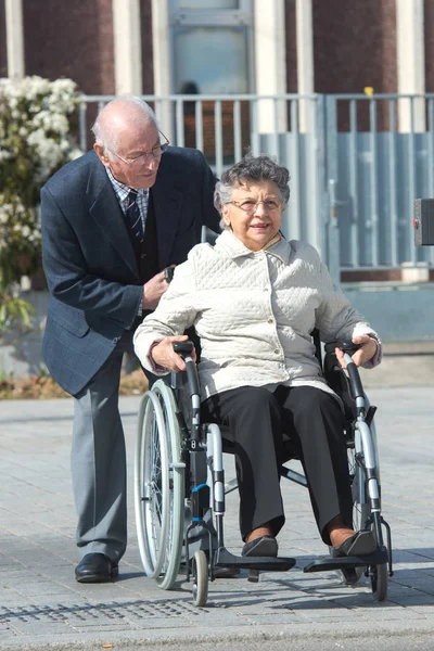 Anziano uomo essere spinto da moglie in sedia a rotelle — Foto Stock