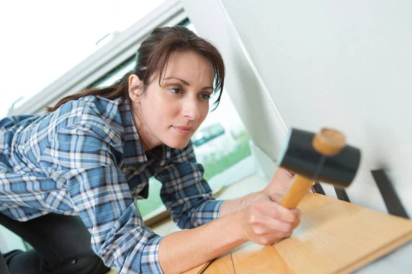 Mooi meisje met een hamer past houten vloer — Stockfoto