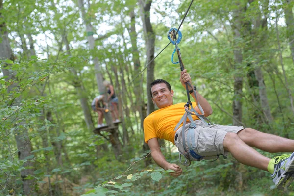 Glimlachende man rijden een zip-lijn in het bos — Stockfoto