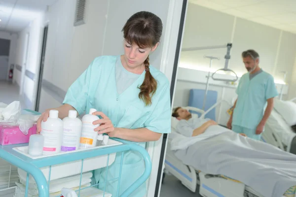 Jonge vrouwelijke verpleegkundige met het schoonmaken van product op trolley in ziekenhuis — Stockfoto