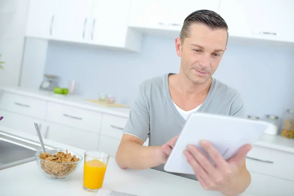 Щасливий чоловік читає новини на планшеті під час сніданку — стокове фото