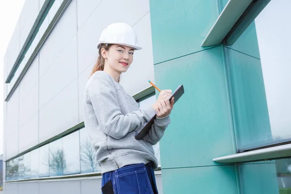 Young woman builder writing something in clipboard at construction site — Stock Photo, Image