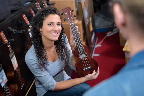 Beautiful girl holding a guitar in a musical shop — Stock Photo, Image