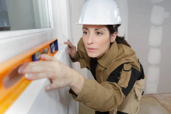 Trabajador femenino de la construcción utilizando una herramienta de nivel en la pared de la casa —  Fotos de Stock