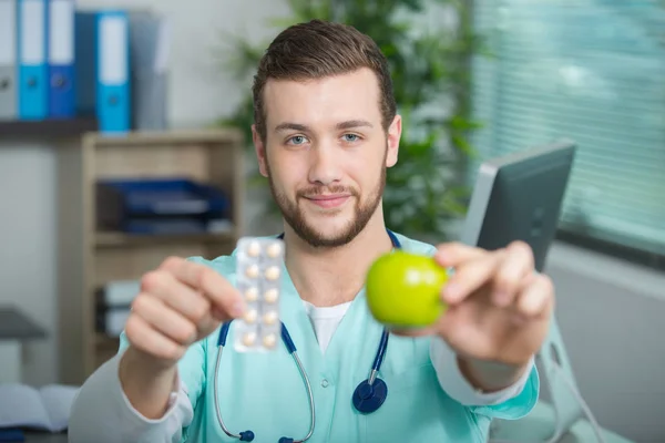 Young doctor showing apple and tablets — Stock Photo, Image