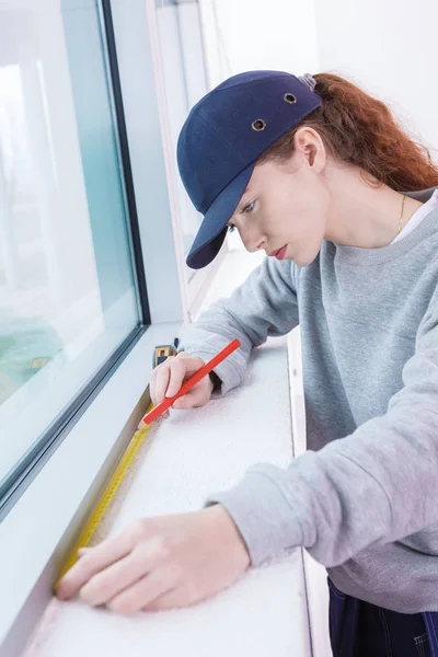 Mujer joven midiendo la pared con cinta métrica — Foto de Stock