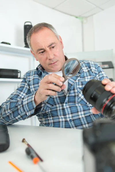 Мужчина ремонтирует камеру на своем рабочем месте на белом фоне — стоковое фото