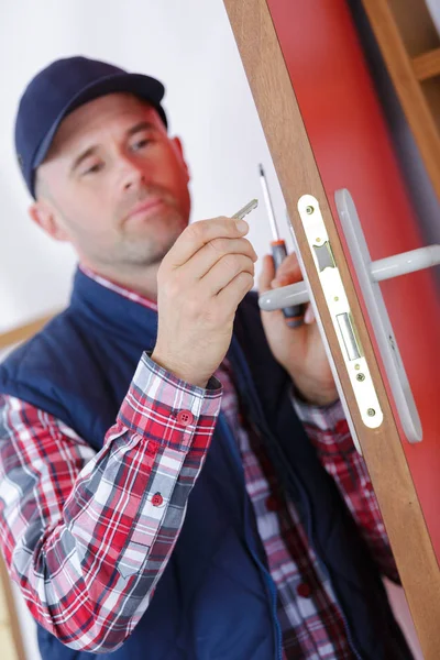 Uomo che fissa la porta con cacciavite — Foto Stock