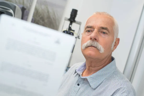 Doctor pidiendo al paciente que lea la historia detrás de él — Foto de Stock