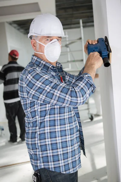 Lavoratore anziano macinazione parete della casa — Foto Stock