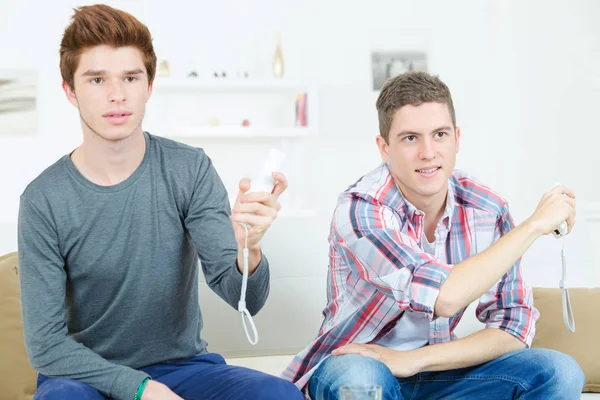 Young men playing video games while sitting on sofa — Stock Photo, Image
