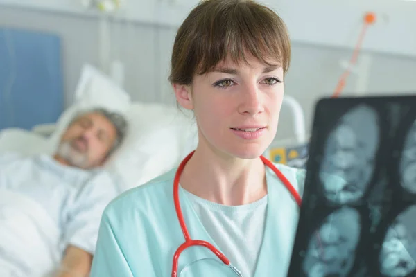 Médico mirando rayos X, paciente en cama de hospital en segundo plano — Foto de Stock