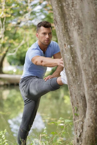 Man stretching his leg on a three — Stock Photo, Image
