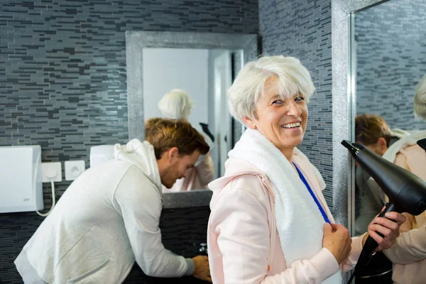 Mulher idosa em banheiro usando secador de cabelo — Fotografia de Stock