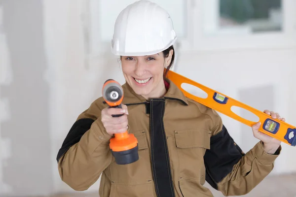 Trabalhador feminino feliz com nível de ferramenta e broca no trabalho — Fotografia de Stock