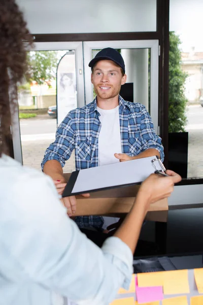 Smiling delivery man and young woman signing clipboard — Stock Photo, Image