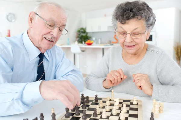 Старшая супружеская пара играет в шахматы дома — стоковое фото
