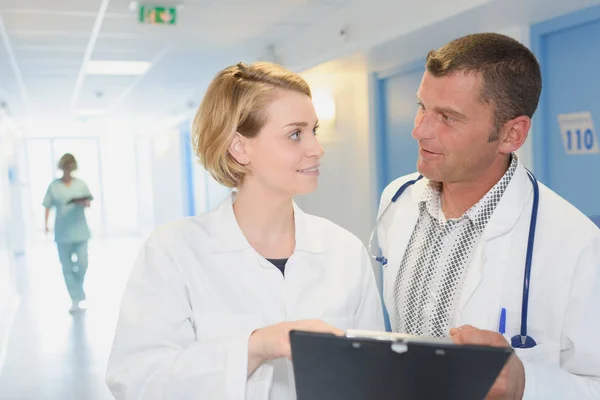 Medici sorridenti con appunti che camminano lungo il corridoio dell'ospedale — Foto Stock