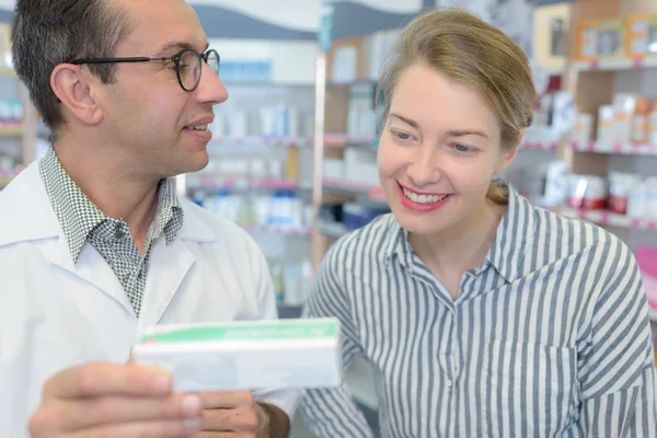 Cliente sonriente y farmacéutico sosteniendo caja de medicamentos en el hospital — Foto de Stock